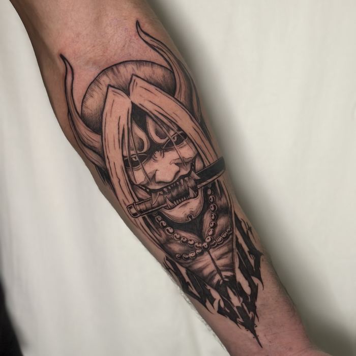 Tatuaje de máscara oni con cuchillo entre los dientes y collar de cuentas